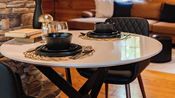A cozy room with a stone wall, a round dining table with black tableware, a ceiling fan, and a window with curtains.