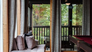 A cozy room with a sofa, a pool table, and a view of a wooden deck and trees.