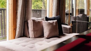 A cozy seating area with a cushioned bench and pillows, large windows with curtains, and a view of trees outside.