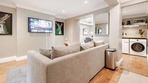 Een moderne woonkamer met een grijze bank, een televisie, een spiegel en een wasruimte.