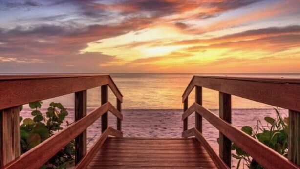 Eine Holzterrasse führt zu einem Strand mit Sonnenuntergang.