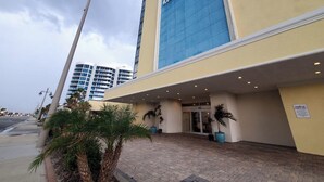 Entrada de hotel con fachada azul, palmeras y un letrero de estacionamiento.