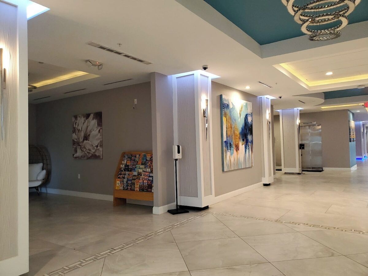 Un'ampia hall dalle linee moderne, con una reception, un'area salotto e un pannello decorato con un dipinto floreale.