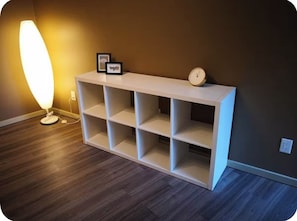 Valkoinen konsolipöytä, jossa on useita hyllyjä, on sijoitettu tummaa seinää vasten. Pöydällä on myös lattiavalaisin ja kello.