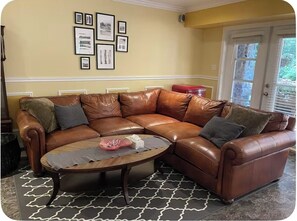 Ruskea nahkasohva, jossa on useita osia, pyöreä sohvapöytä, kuviollinen matto ja seinällä olevia kehystettyjä tauluja.