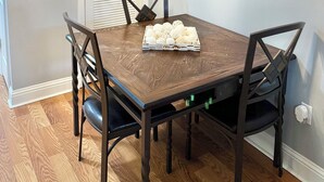 A dining area with a wooden table, four chairs, a chandelier, a door, and a painting on the wall. - Recently Updated Trendy Biloxi Beach Condo (Biloxi)