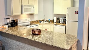 A kitchen with white cabinets, a granite countertop, a microwave, stove, and dishwasher. - Recently Updated Trendy Biloxi Beach Condo (Biloxi)