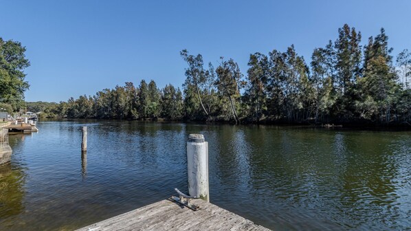 A wooden dock extending into a calm river, surrounded by dense trees and clear skies.