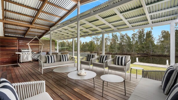 Eine überdachte Terrasse im Freien mit Holzboden, gepolsterten Sitzmöbeln und einem Grill.