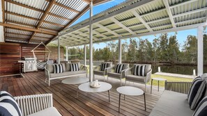 A covered outdoor deck with wooden flooring, cushioned seating, and a grill.