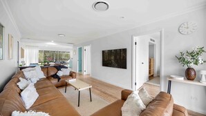 Ein geräumiges Wohnzimmer mit einer großen braunen Ledersofa, einem Couchtisch und einem Waldgemälde an der Wand.
