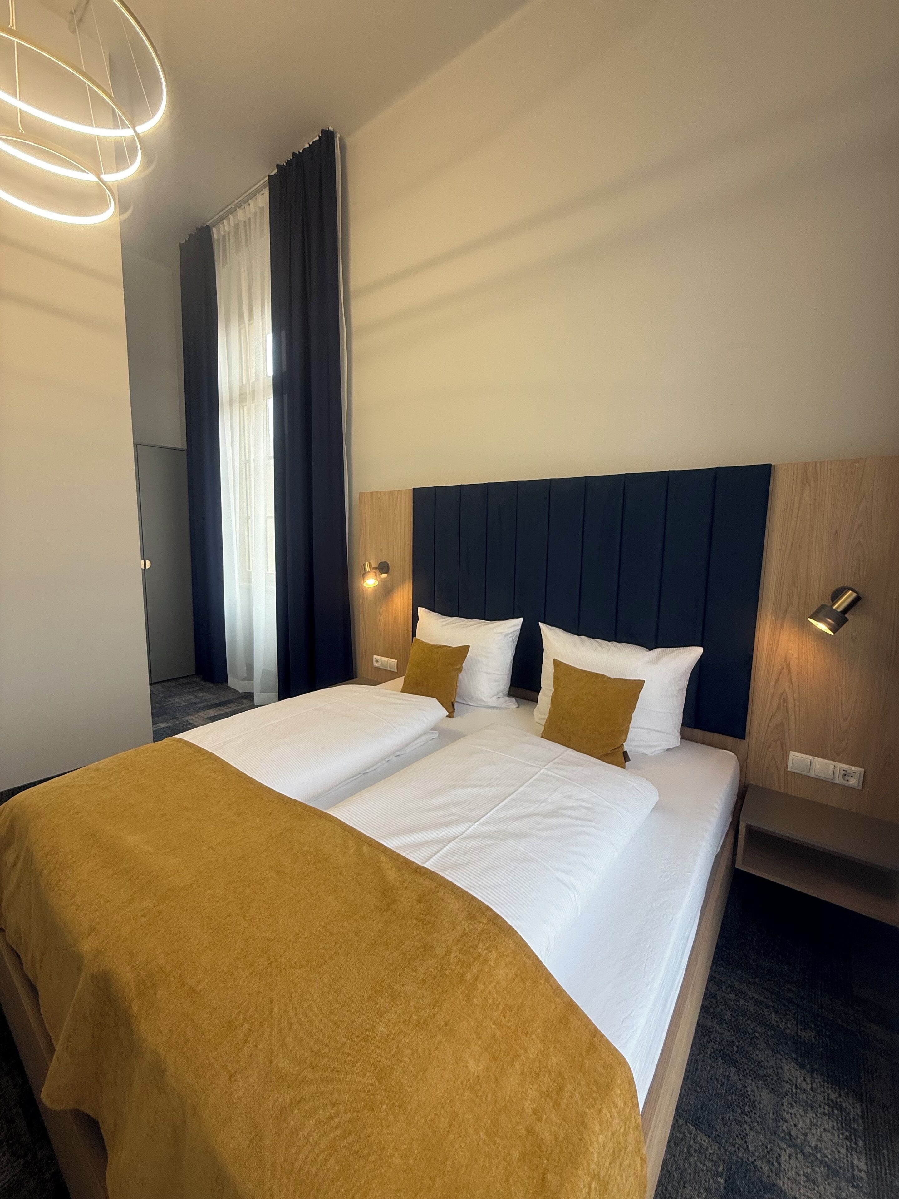 Een hotelkamer met twee bedden, een donker hoofdbord en een moderne lamp.