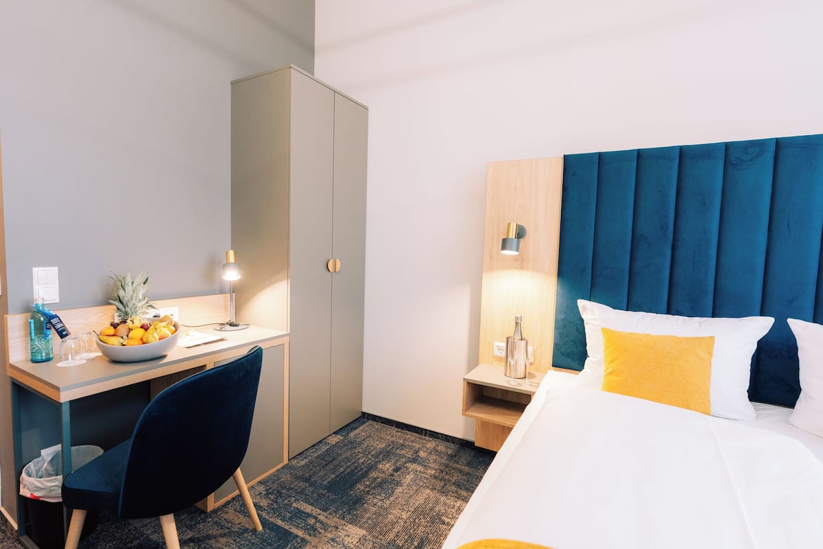 A hotel room with a bed, a desk with a bowl of fruit, a chair, a nightstand, and a lamp.