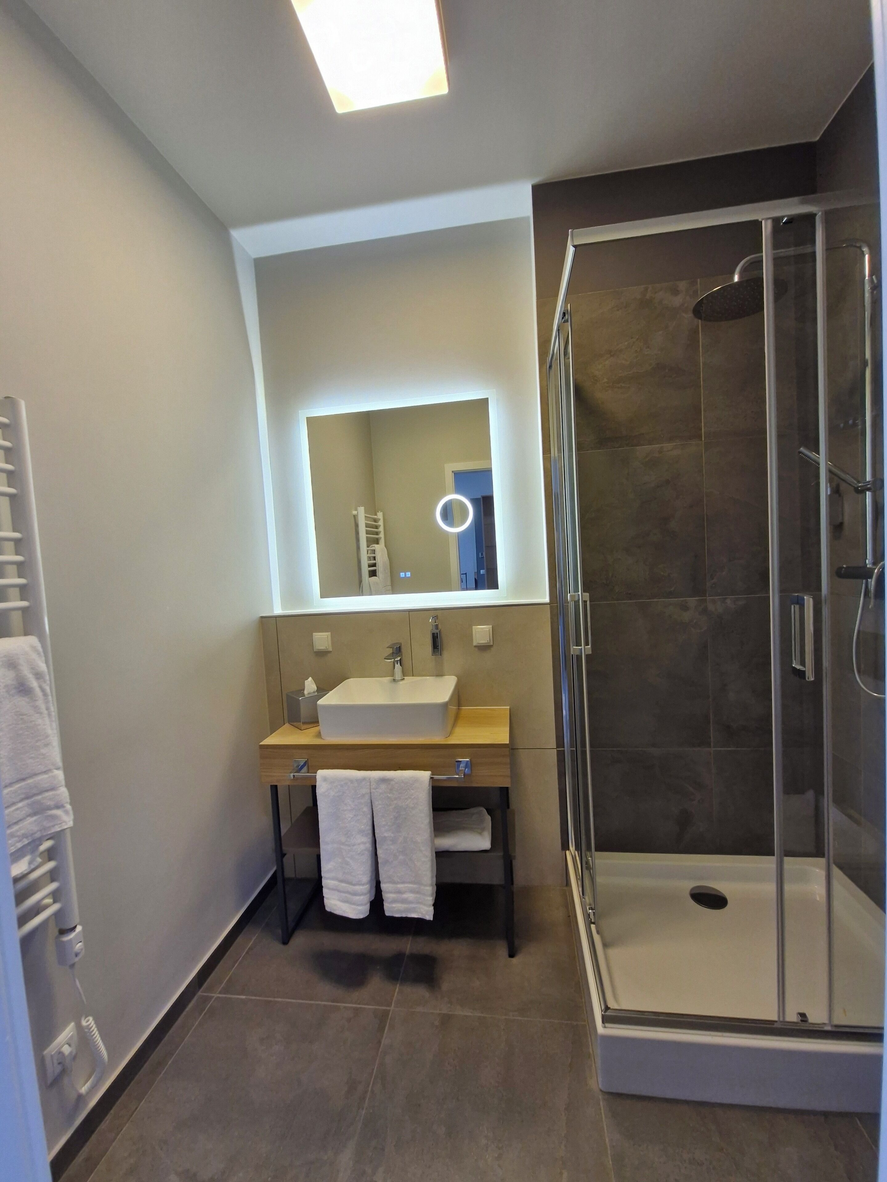 Un baño moderno con ducha envuelta en vidrio, un espejo grande y un mueble de tocador de madera.