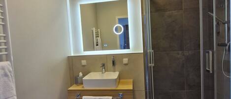 Un baño moderno con ducha envuelta en vidrio, un espejo grande y un mueble de tocador de madera.