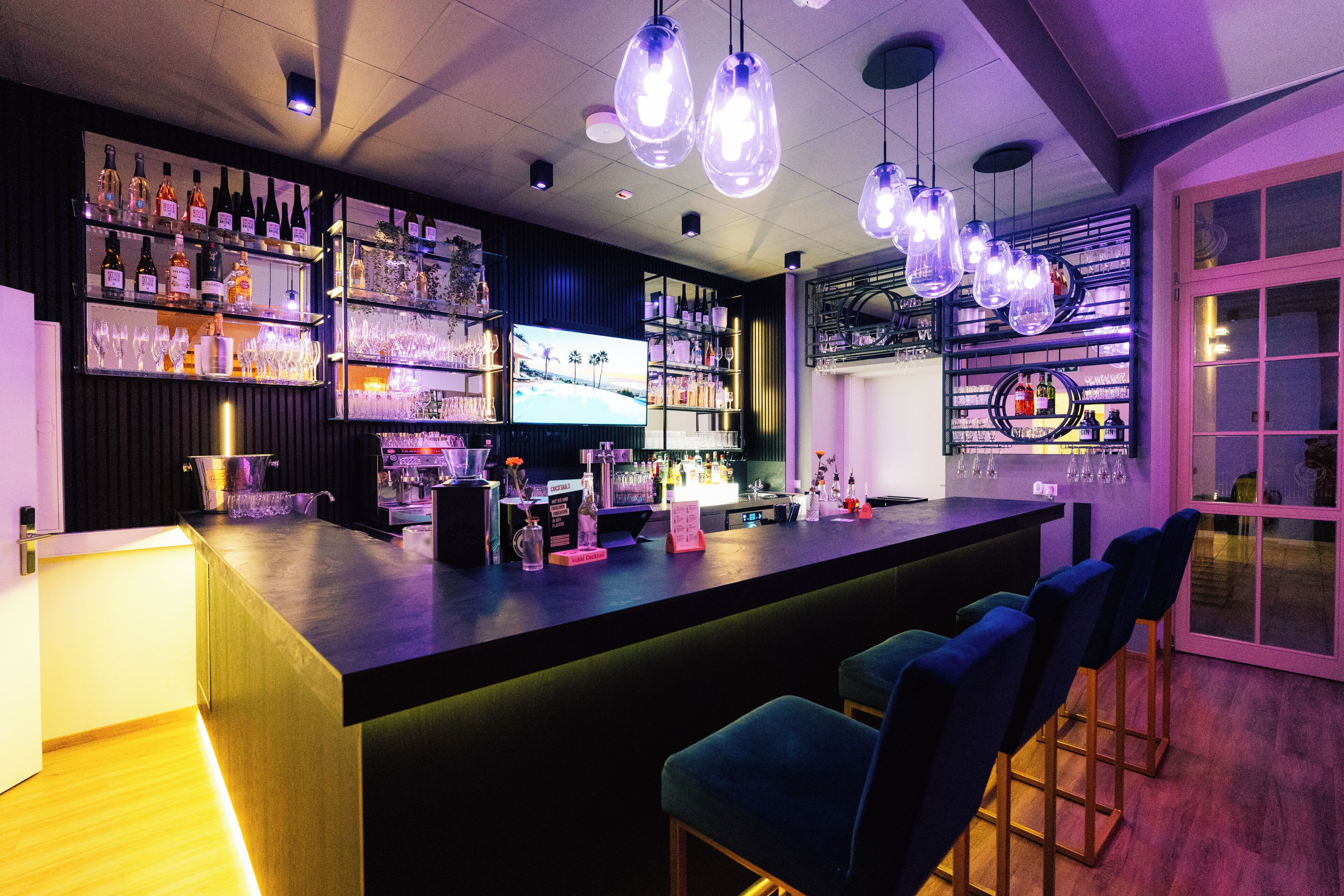 A bar area with shelves of bottles, glasses, and a television screen.