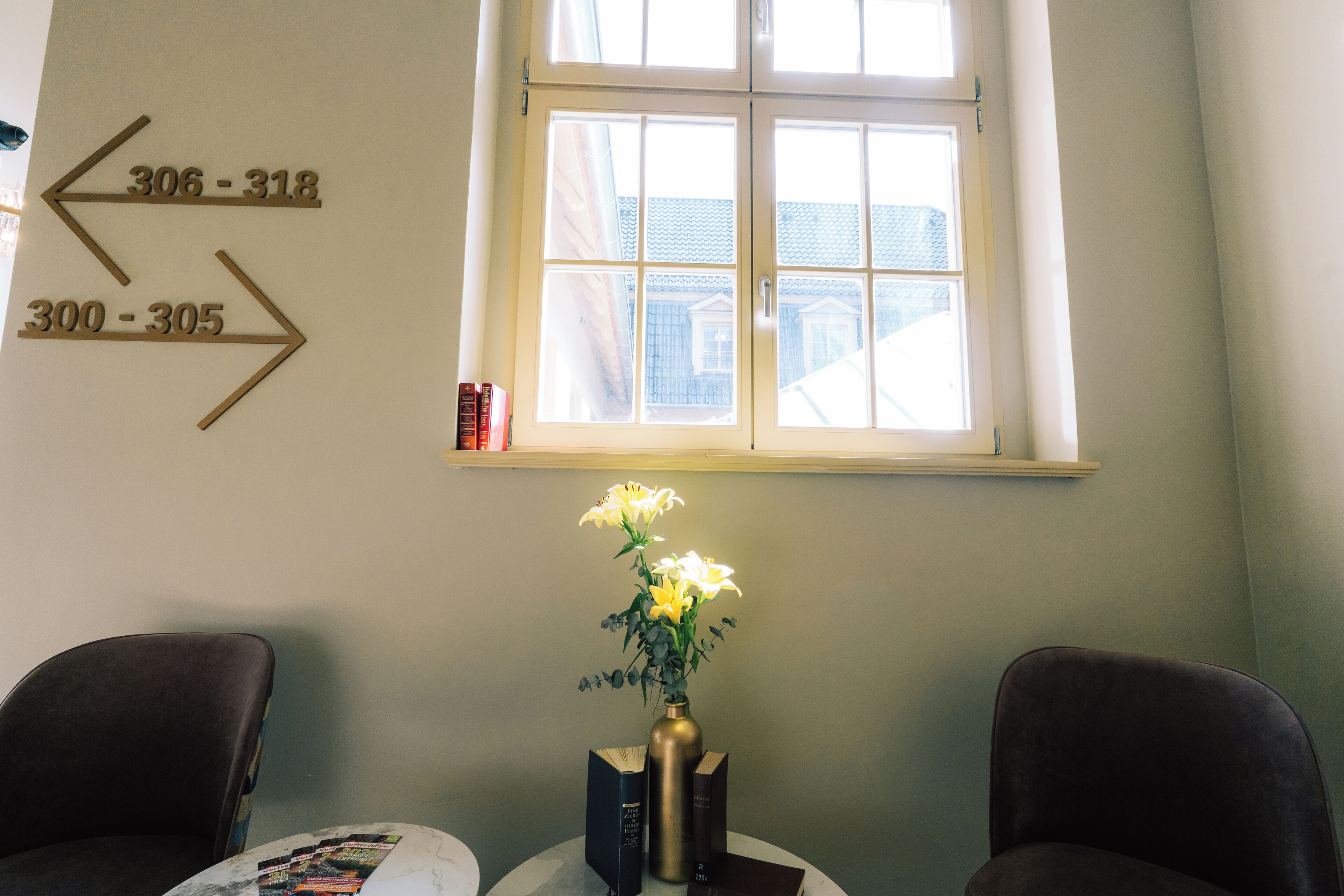 A room with directional signs, a window with a view, a vase with flowers, and two chairs.