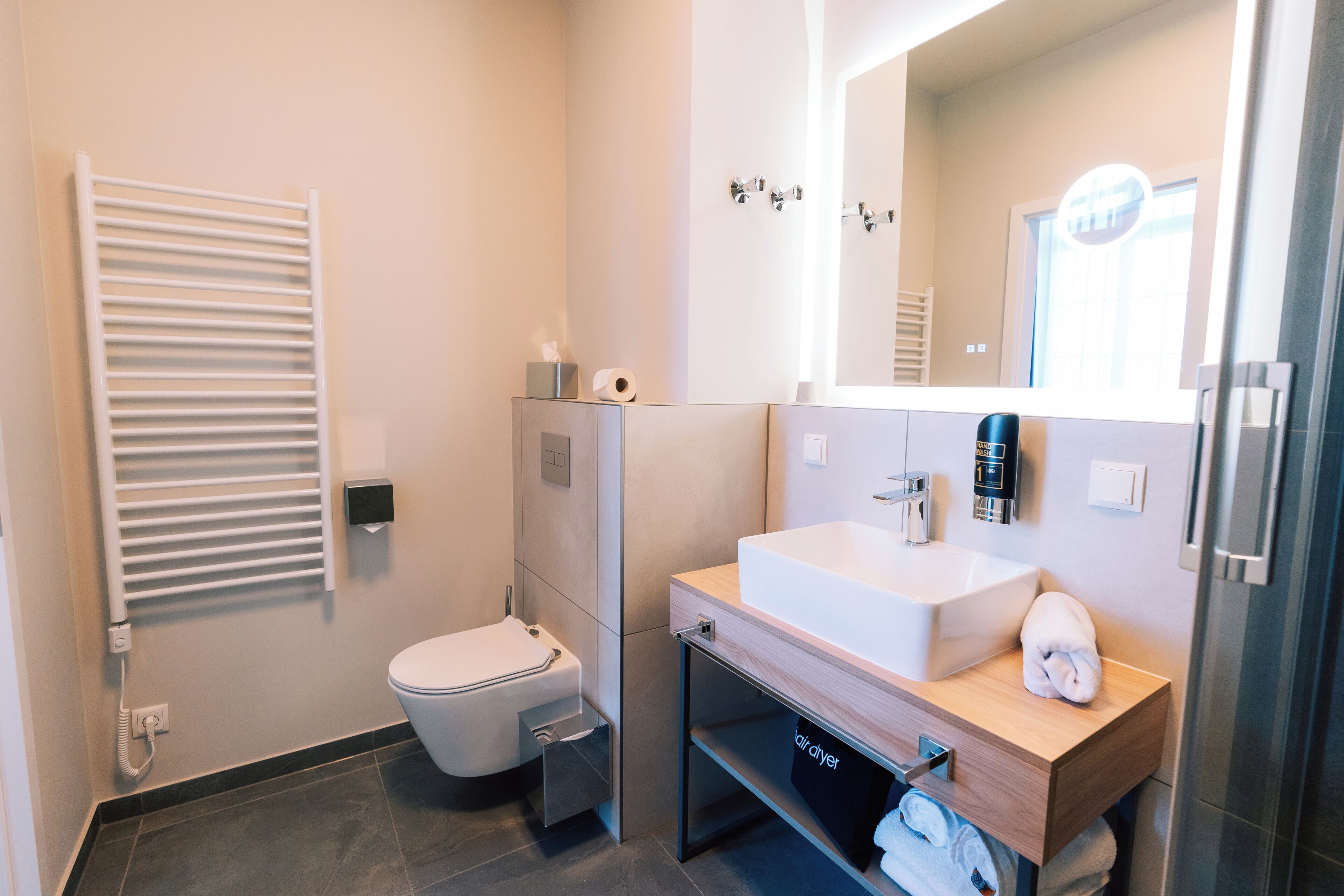 A modern bathroom with a toilet, a sink, a towel rack, and a mirror.