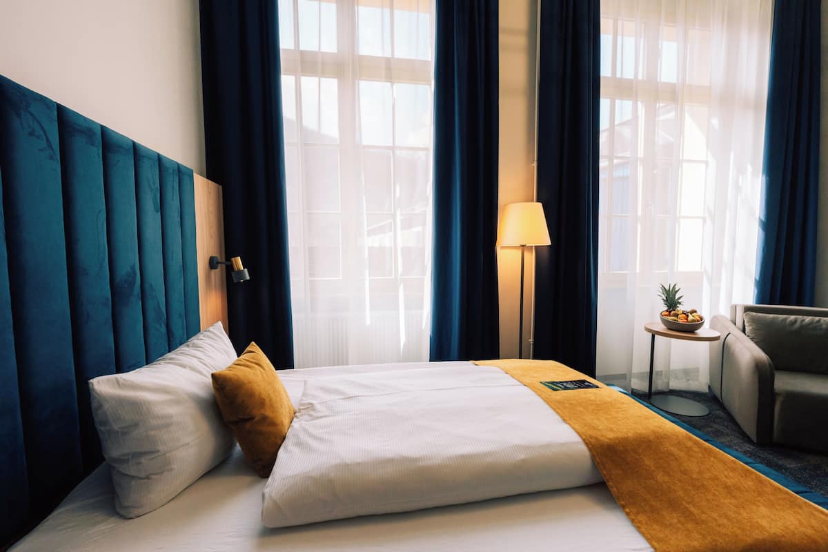 A hotel room with a bed, a nightstand, a lamp, a chair, and a window with curtains.