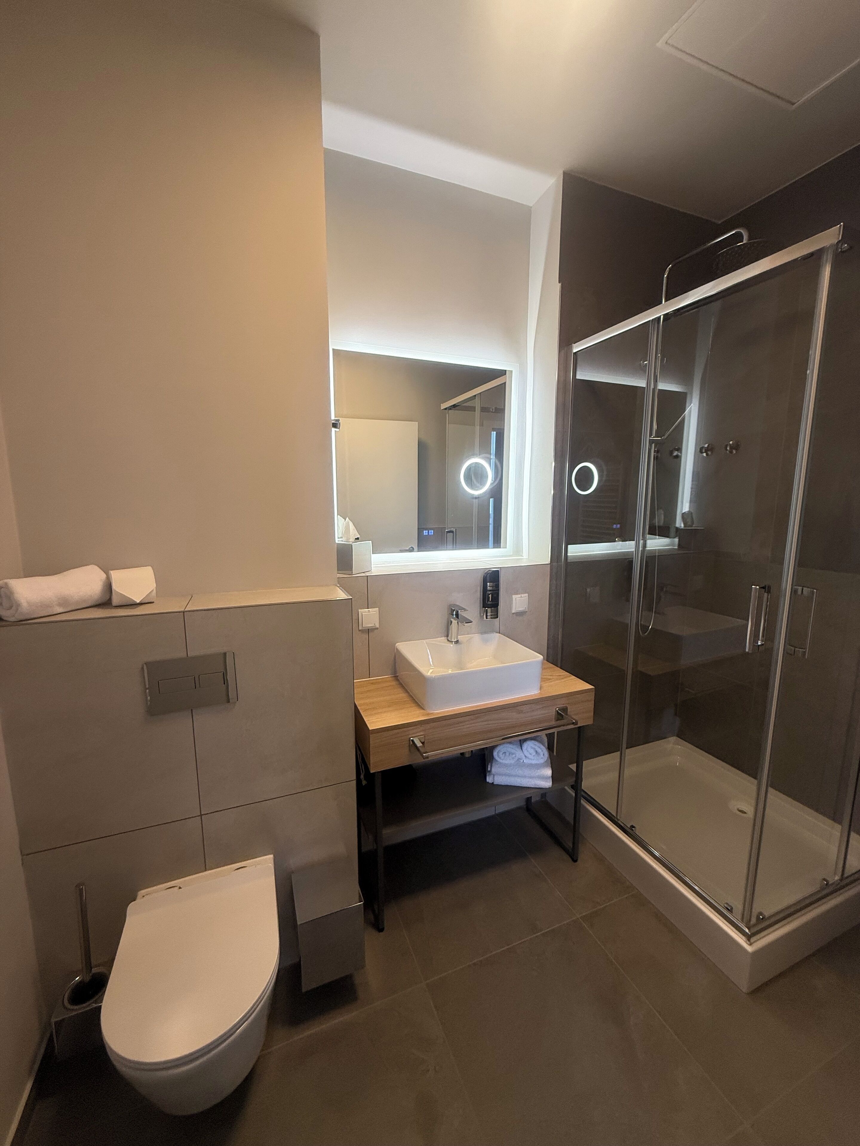 Un baño moderno con cabina de ducha de vidrio, un lavabo blanco y un inodoro.