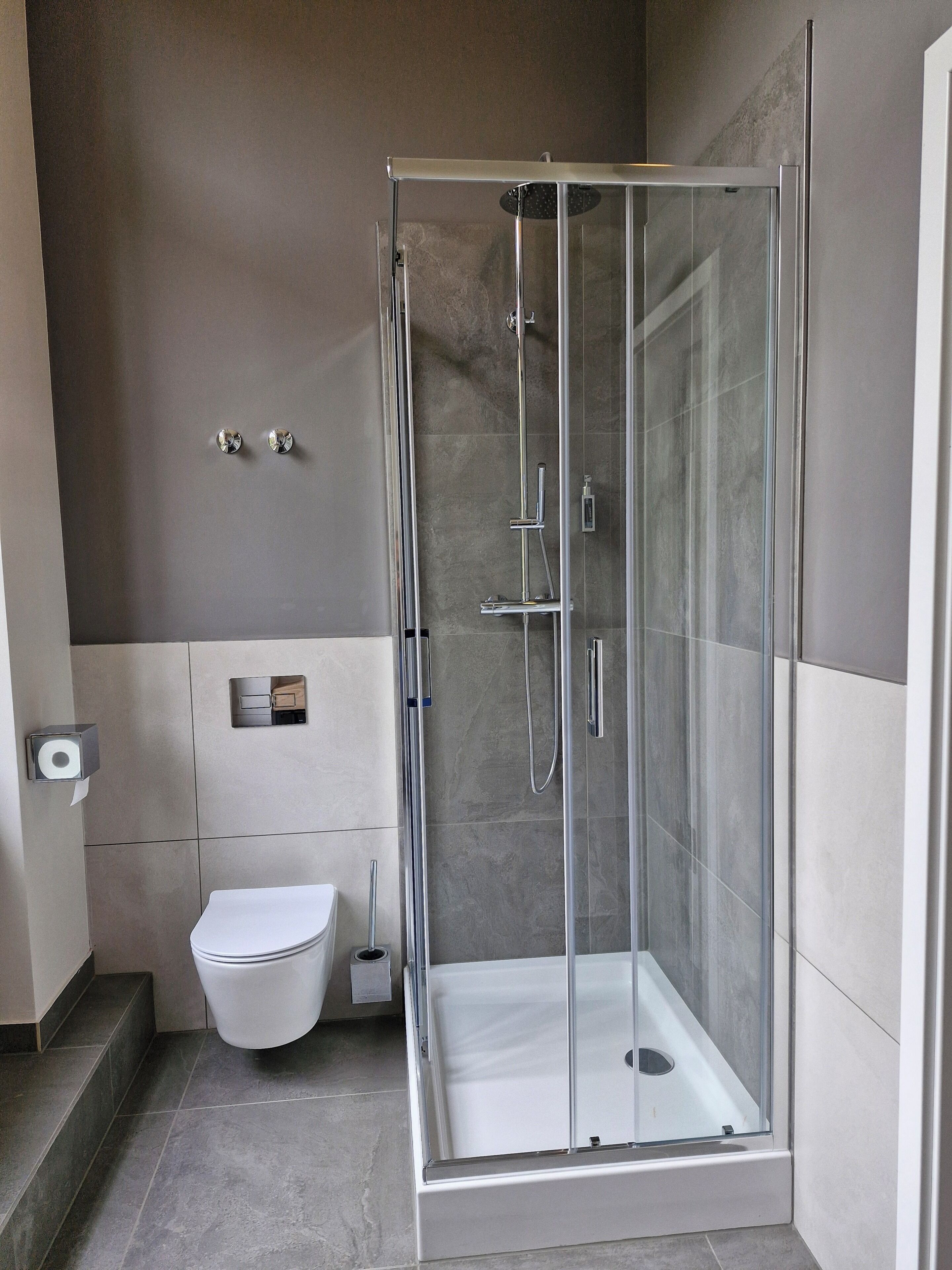 A modern bathroom with a glass-enclosed shower, a toilet, and a towel dispenser.