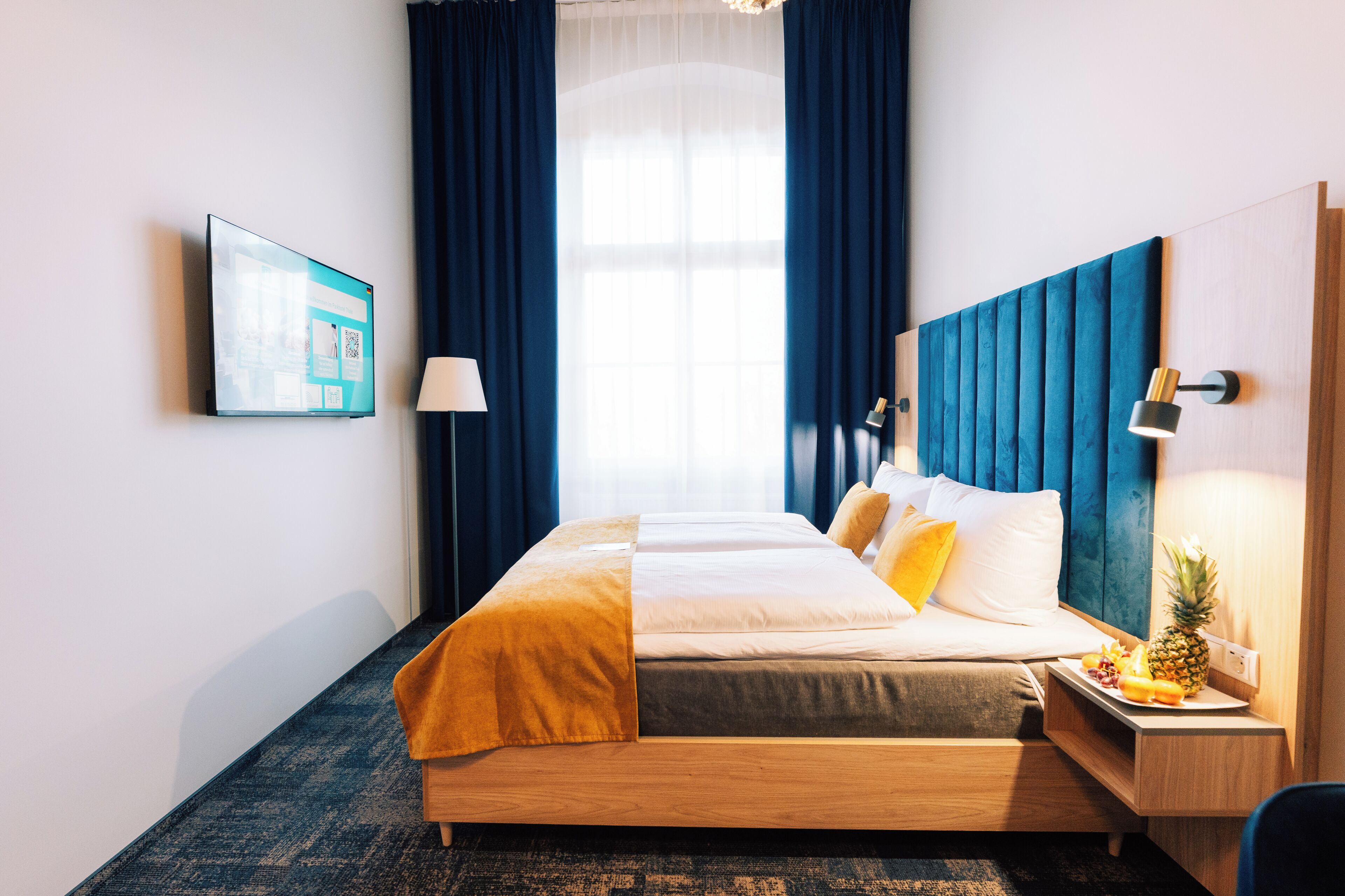 A hotel room with a bed, a nightstand, a lamp, a fruit plate, and a wall-mounted TV.