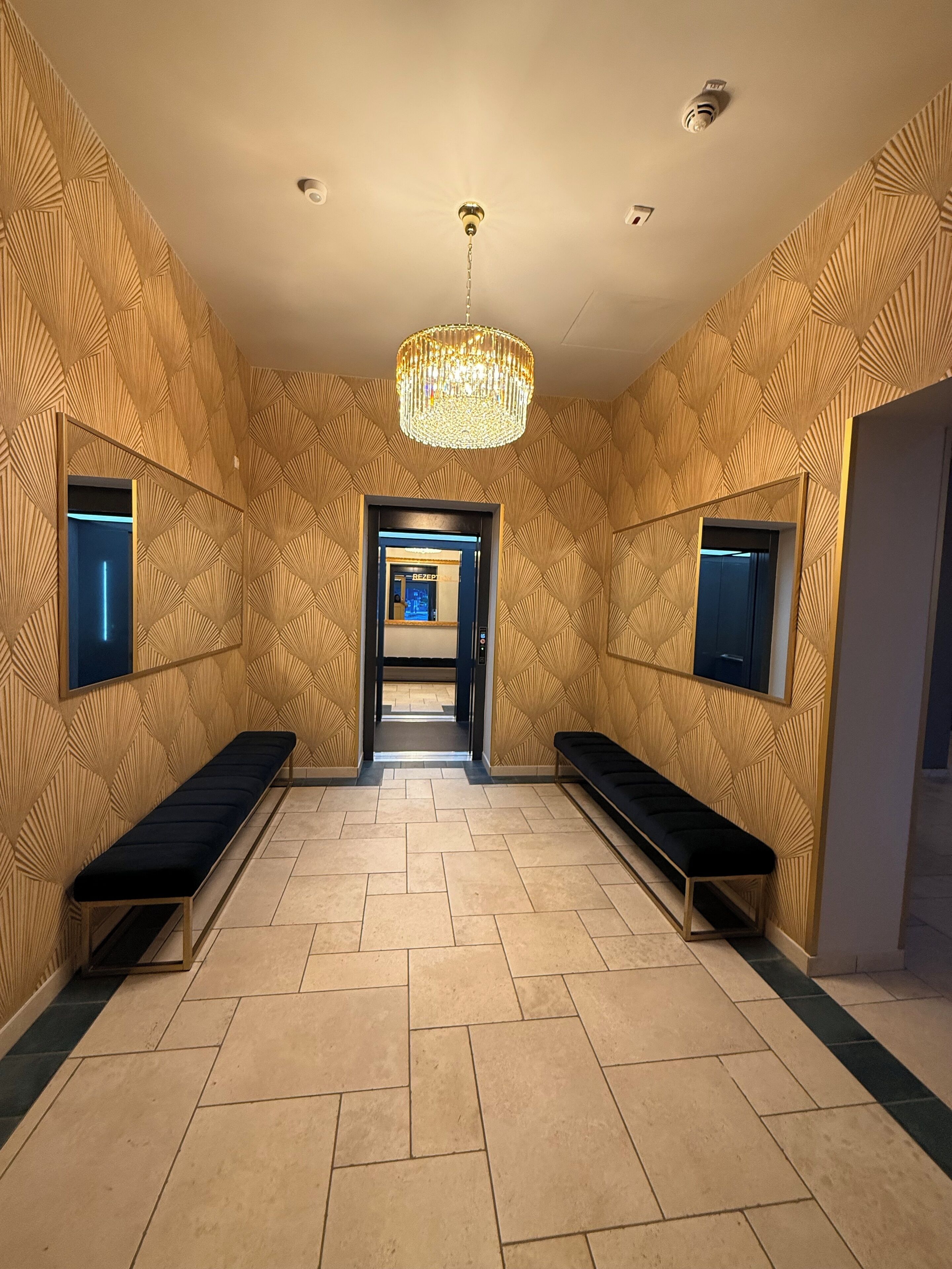 A hallway with patterned walls, a chandelier, and benches.