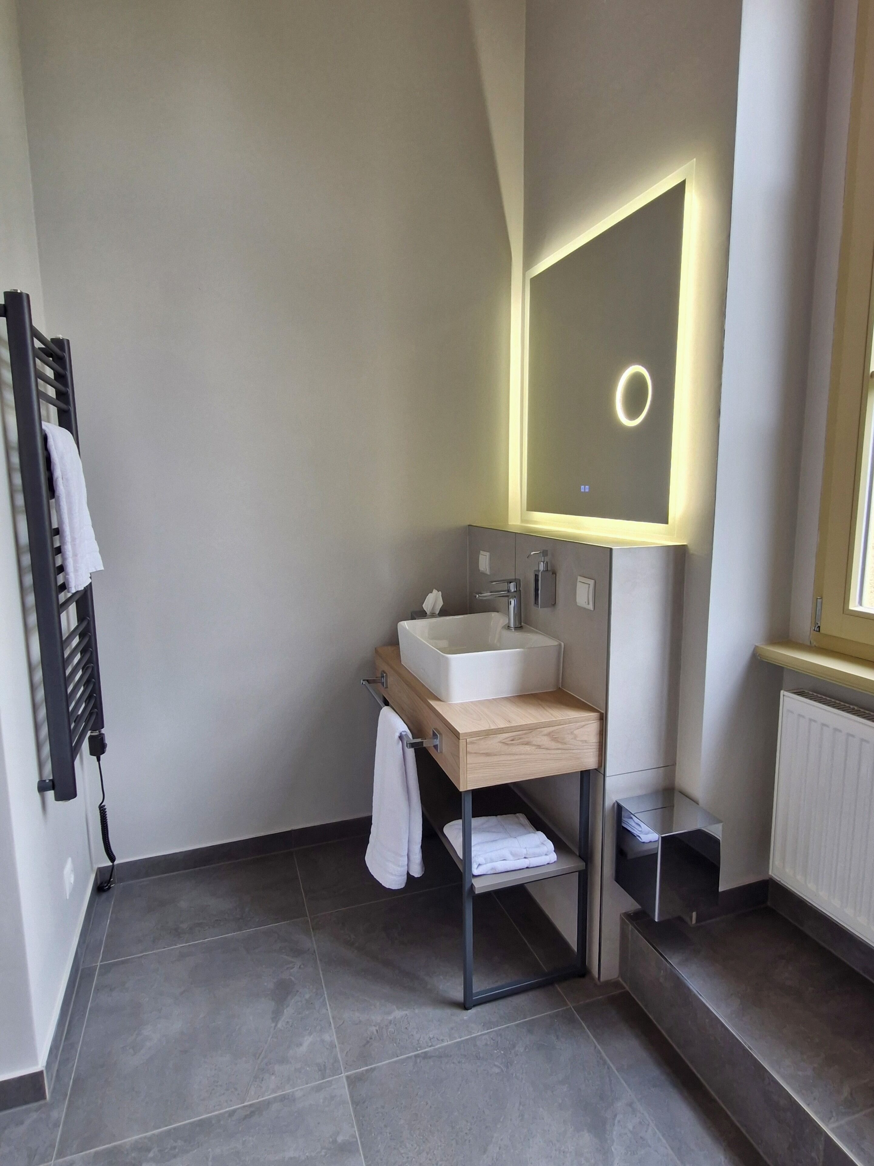 Ein modernes Badezimmer mit einem rechteckigen Waschbecken, einem Spiegel mit Beleuchtung, einem Handtuchhalter und einer Heizung.