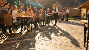 An outdoor dining area with tables and chairs, a green vehicle, and a building in the background. - H24 Parkhotel Thale (Thale)