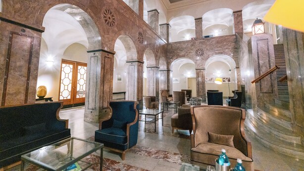 A spacious lobby with high ceilings, marble columns, and a central seating area with armchairs and a glass coffee table. - H24 Parkhotel Thale (Thale)