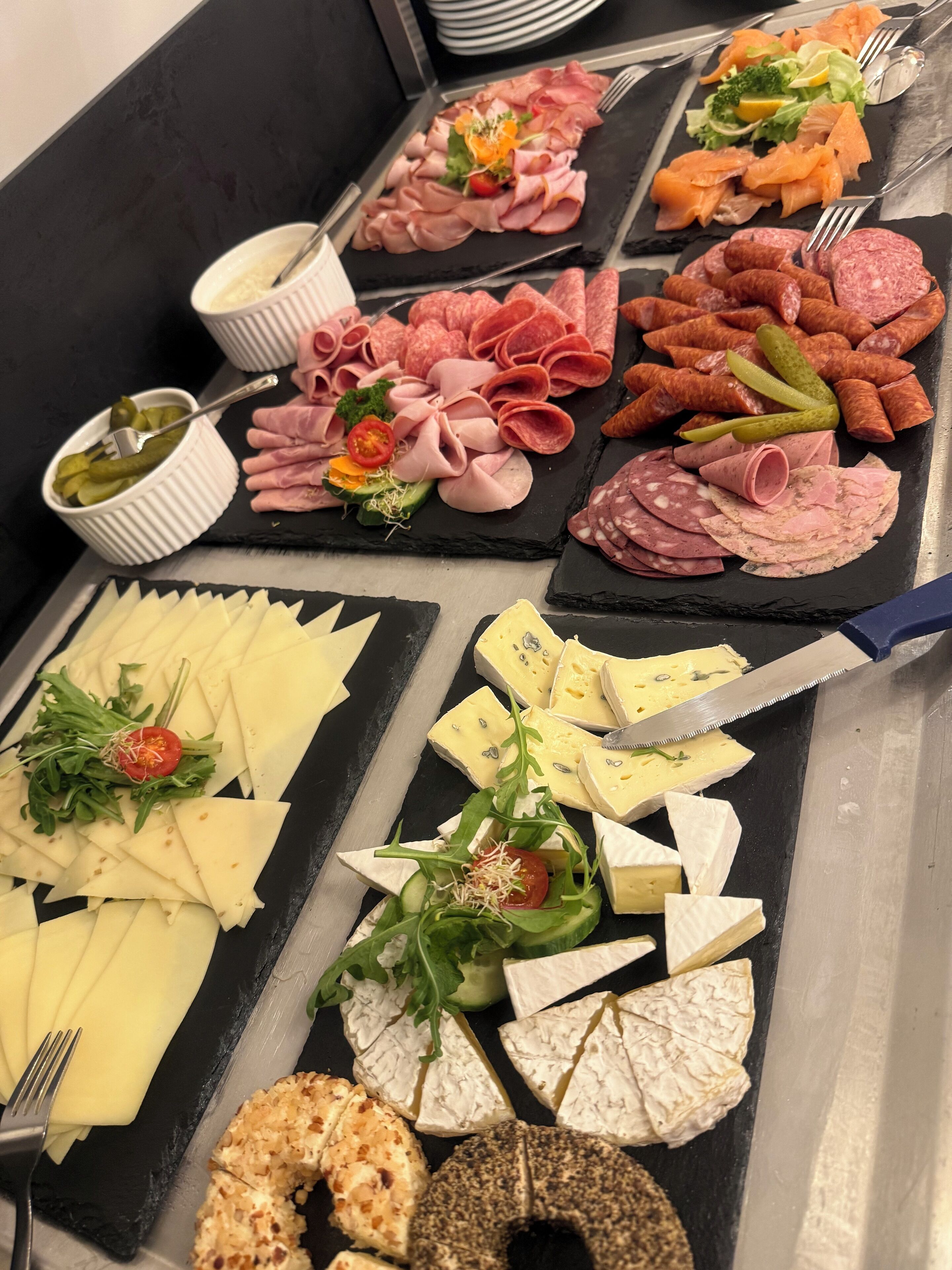 A variety of cheeses, meats, and pickles arranged on black slate boards.