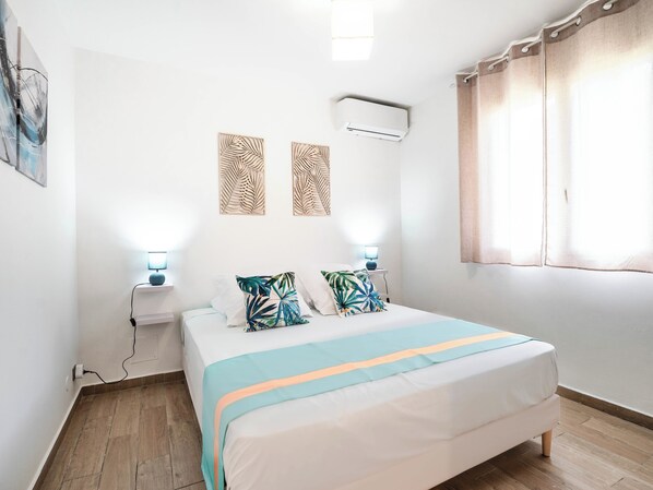 Een slaapkamer met een bed, nachtlampjes, een airconditioner en een raam met gordijnen.