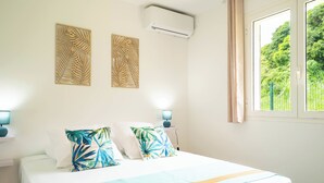Een slaapkamer met een bed, twee wandairconditioners, een raam met uitzicht op groen en twee wandlampen.