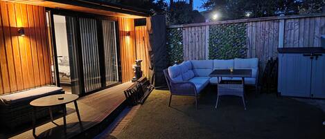 A cozy outdoor patio with a wooden deck, a cushioned seating area, and a table.