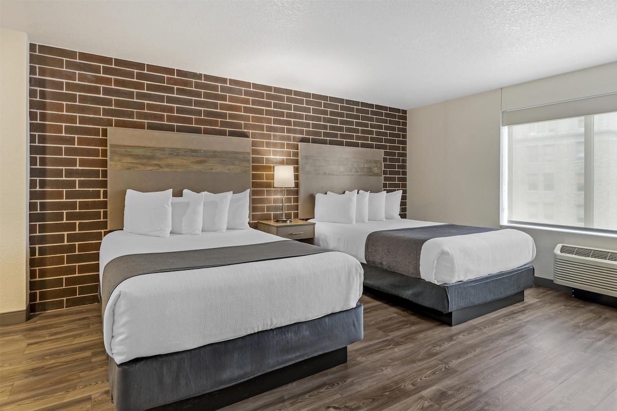 Habitación de hotel con dos camas, un muro decorativo de ladrillo, un ventanal grande y un diseño moderno.