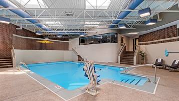 An indoor swimming pool with a clear view of the pool area, a staircase leading to a second level, and a seating area with chairs and a table.