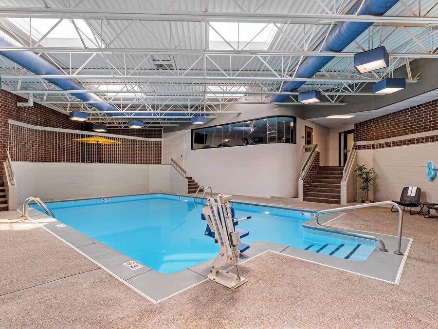 An indoor swimming pool with a clear view of the pool area, a staircase leading to a second level, and a seating area with chairs and a table.