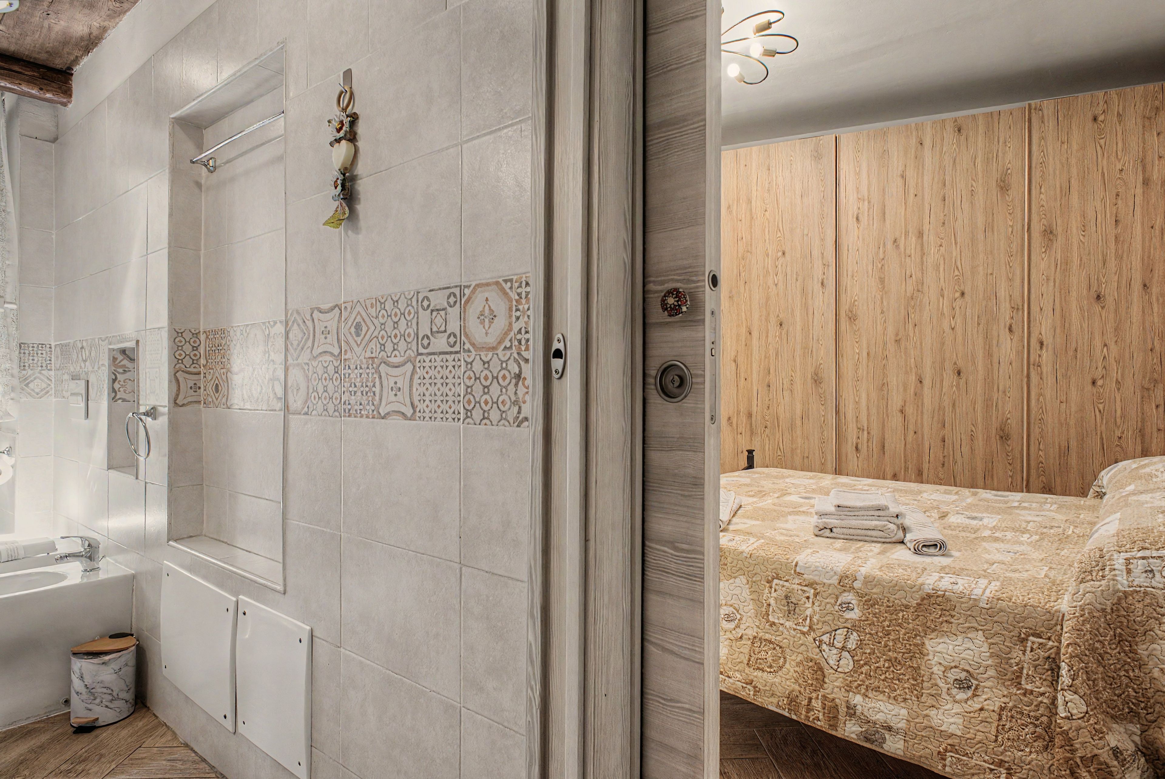 Un bagno con doccia, WC e lavandino. Una porta in legno conduce a una camera da letto con un letto e un'armadio in legno.