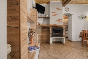 A cozy living room with a fireplace, wooden walls, a television mounted on a wooden beam, and a herringbone-patterned floor.