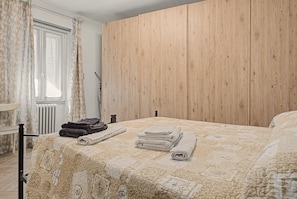 Un dormitorio con cabecera de madera, cama con edredón estampado y ventana con cortinas.