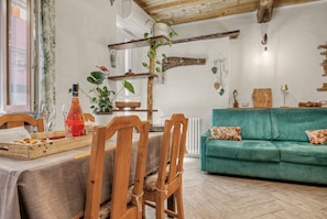 Ein gemütliches Wohnzimmer mit einem Holzesstisch, Stühlen, einem grünen Sofa und einem Holzregal mit Pflanzen.