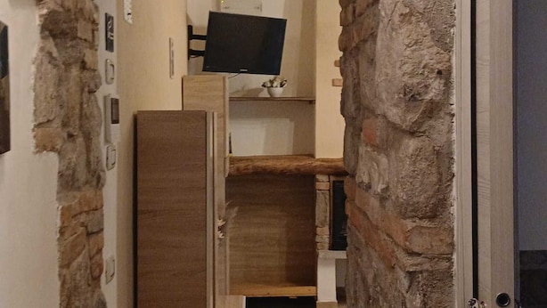 A hallway with stone walls, a wooden door, and a flat-screen TV mounted on a shelf.