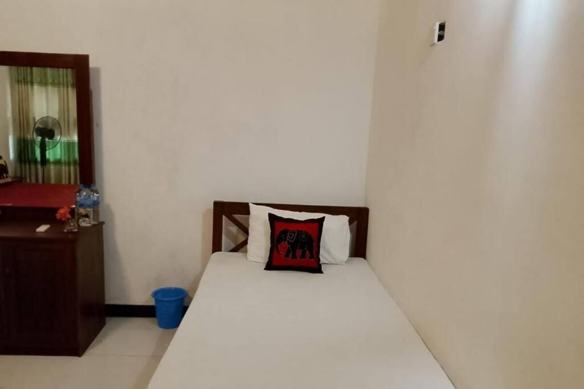 A bedroom with a bed, a wooden headboard, a nightstand, a mirror, and a blue trash bin.
