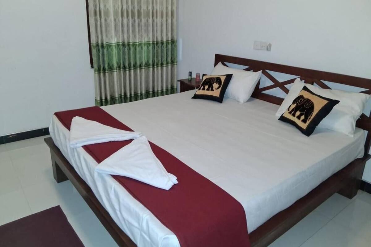 A neatly made bed with a red and white bedspread, two pillows with elephant designs, and a green patterned curtain.