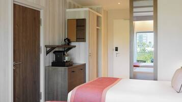 A hotel room with a bed, a desk with a coffee machine, a mirror, and a view of the outdoors.