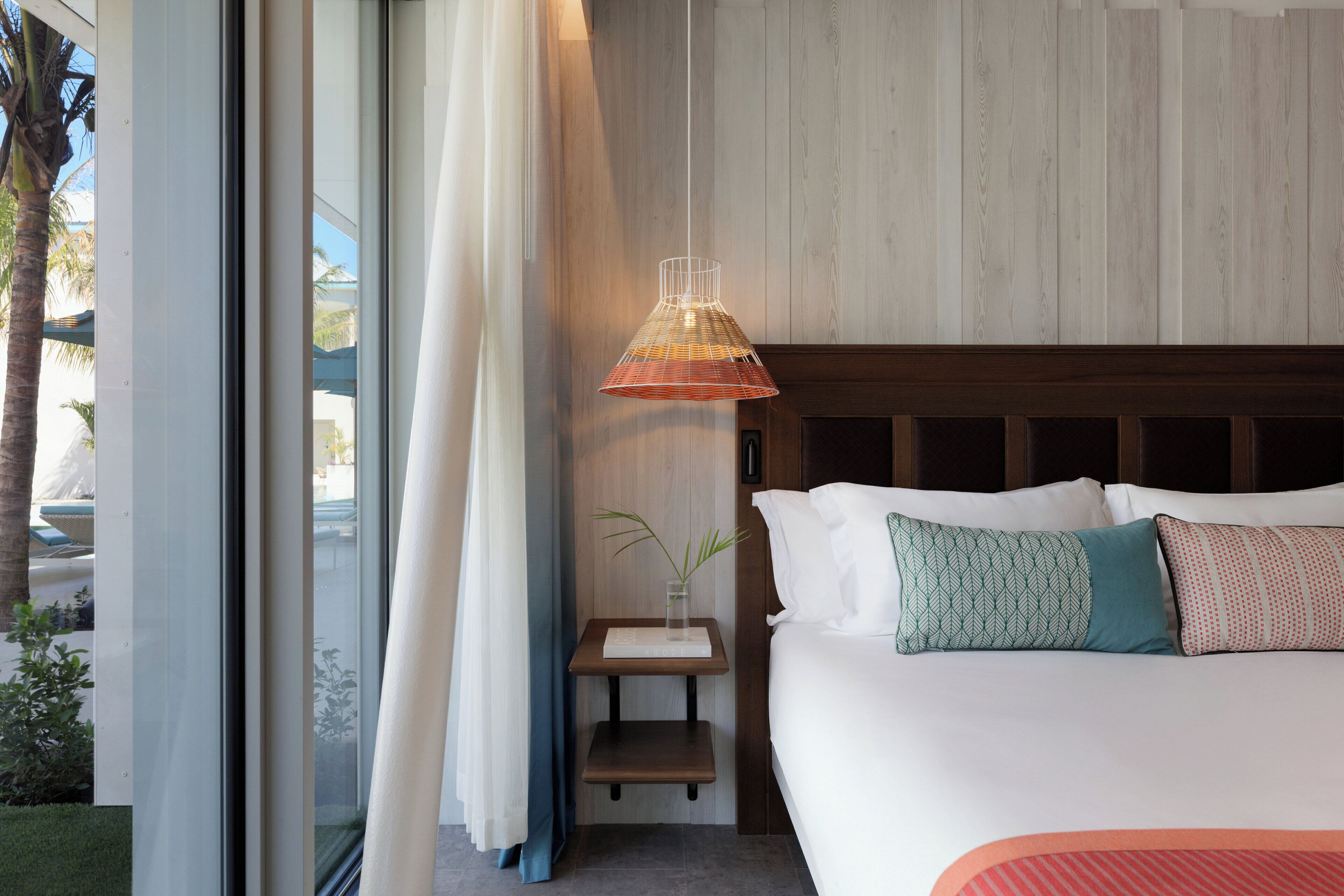 A bedroom with a bed, a bedside table, a lamp, and a view of the outdoors.