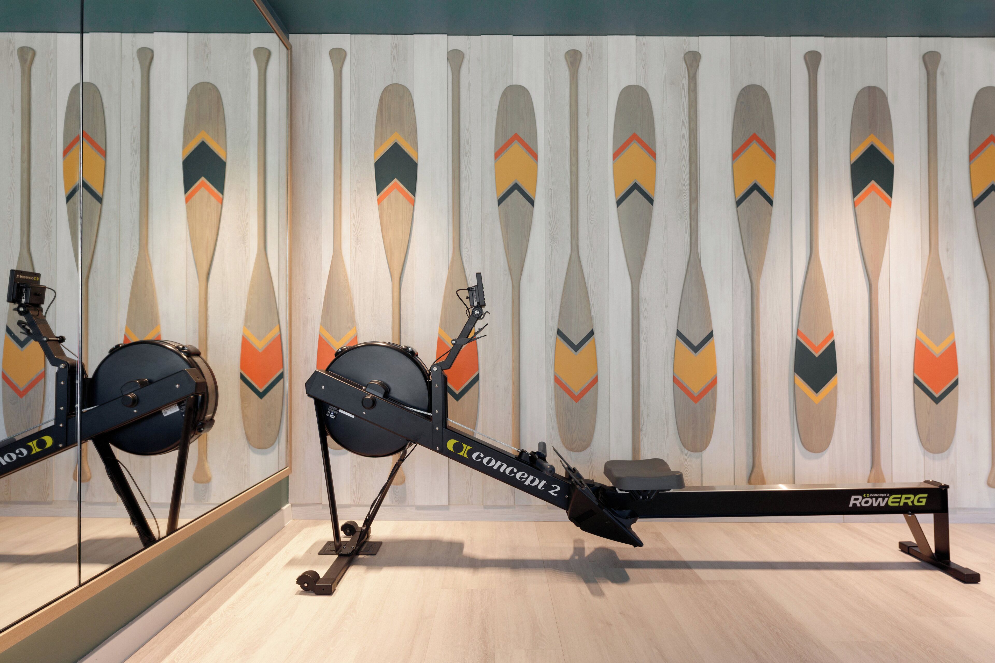 A rowing machine in a room with a mirrored wall and decorative paddles.