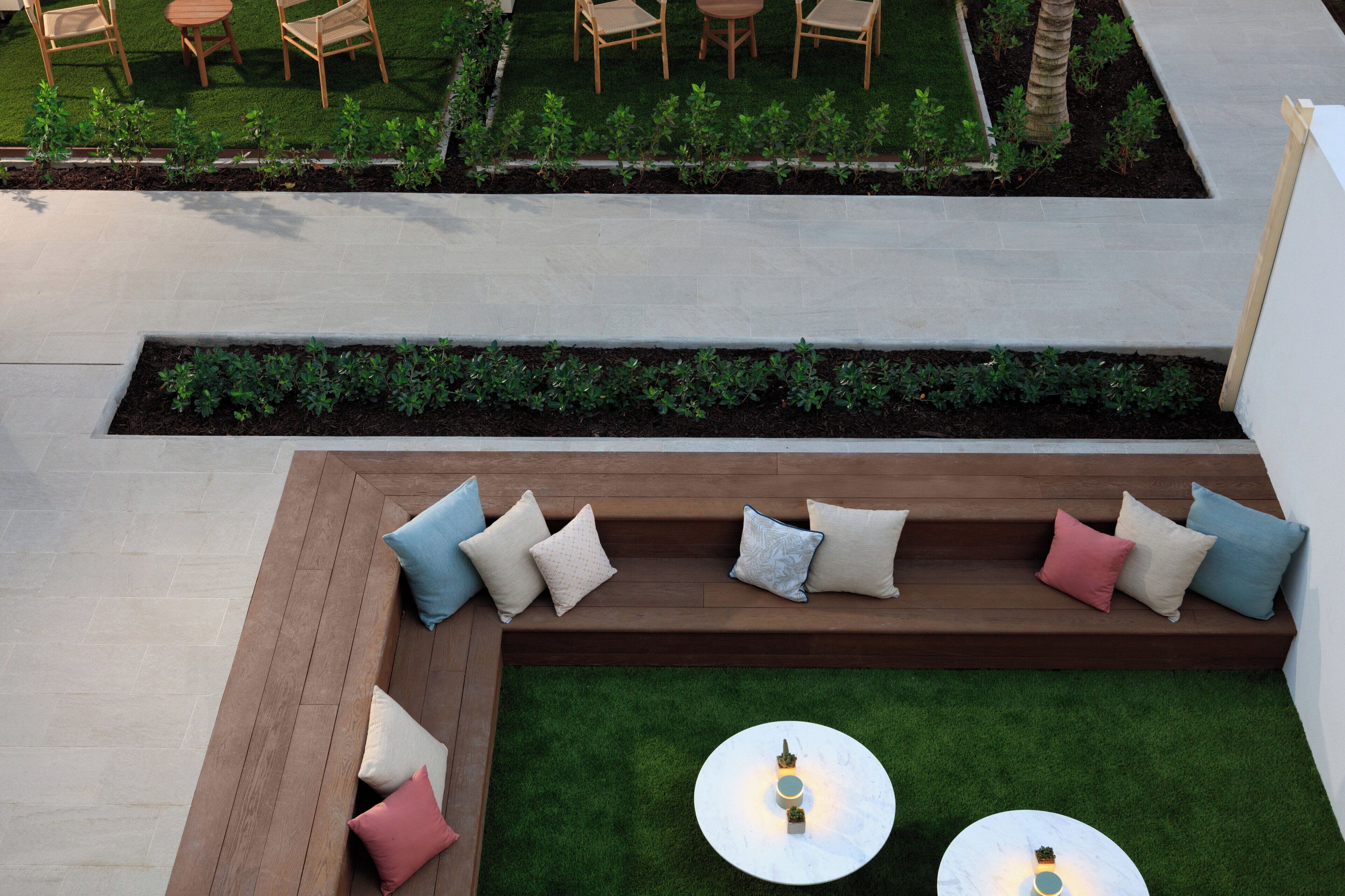 A rooftop terrace with a wooden bench, two round tables, and a small garden area.