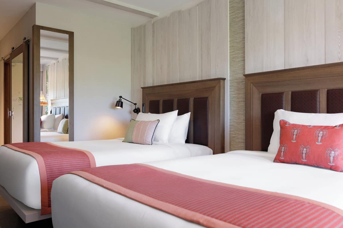 A hotel room with two beds, a mirror, a nightstand, and a lamp.