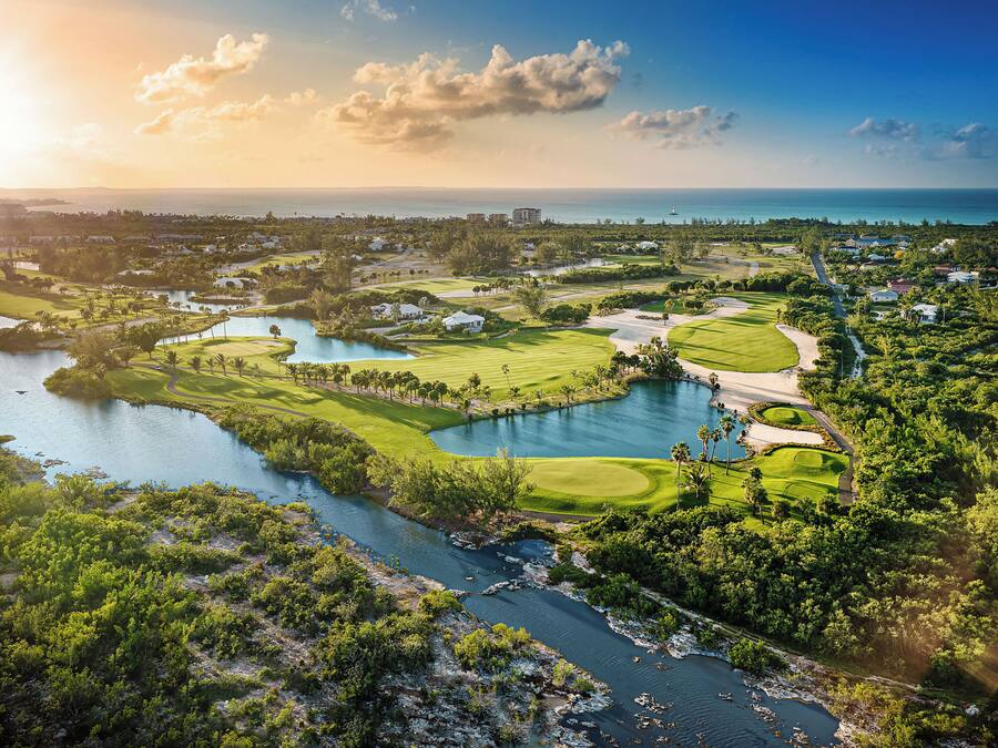 Um campo de golfe com um lago, rodeado por vegetação e edifícios.